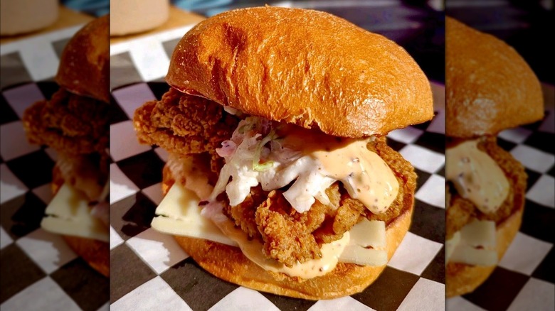 A fried chicken sandwich with coleslaw, cheese, and creamy sauce on a toasted bun
