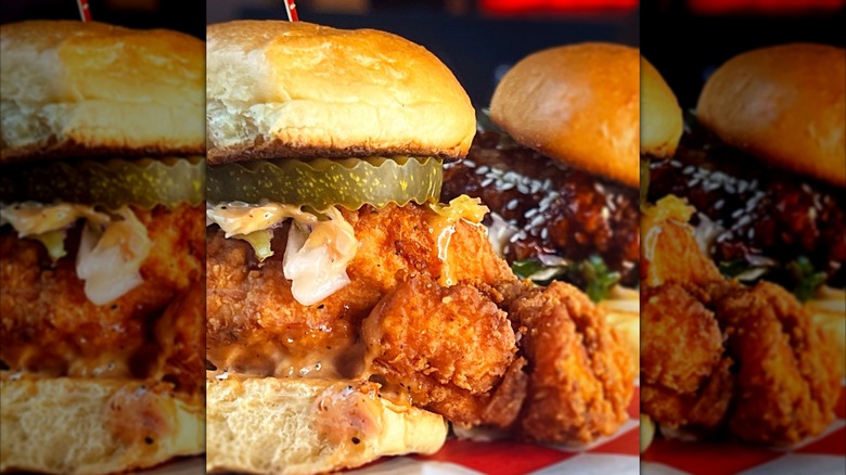 A fried chicken sandwich topped with pickles, coleslaw, and creamy sauce on a checkered tray