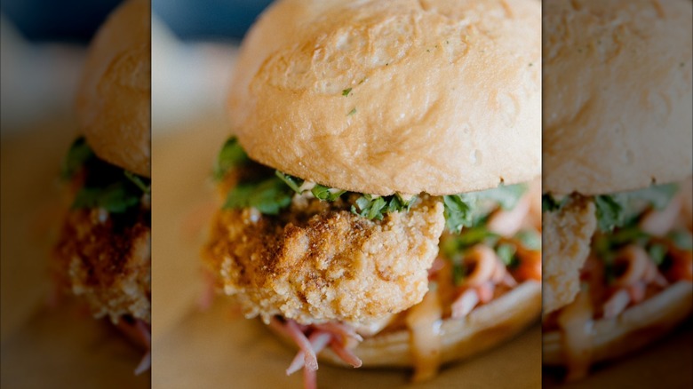 A fried chicken sandwich topped with lettuce and slaw on a rustic bun