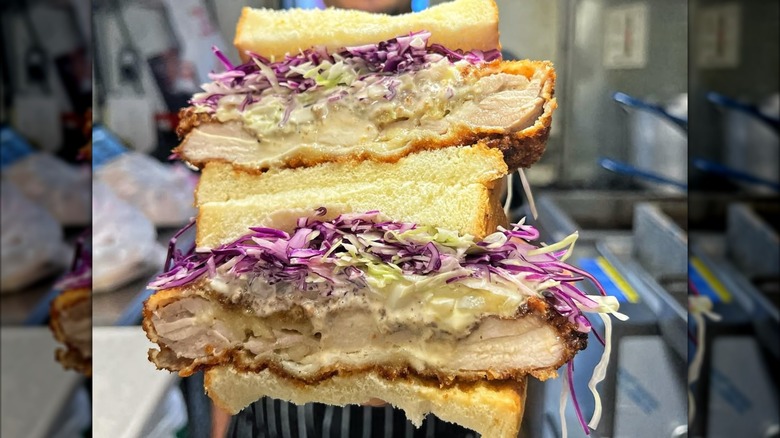 Two stacked fried chicken sandwich halves filled with shredded cabbage and creamy sauce