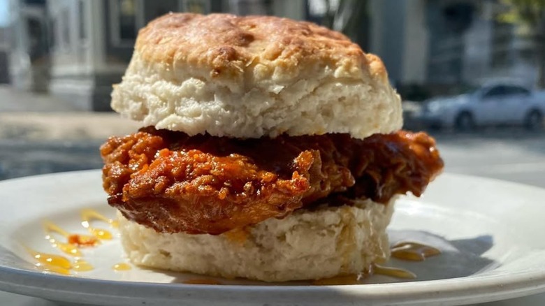 A fried chicken biscuit sandwich drizzled with honey on a white plate
