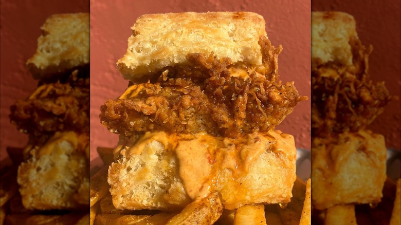 A fried chicken biscuit sandwich covered in sauce and served on top of seasoned fries