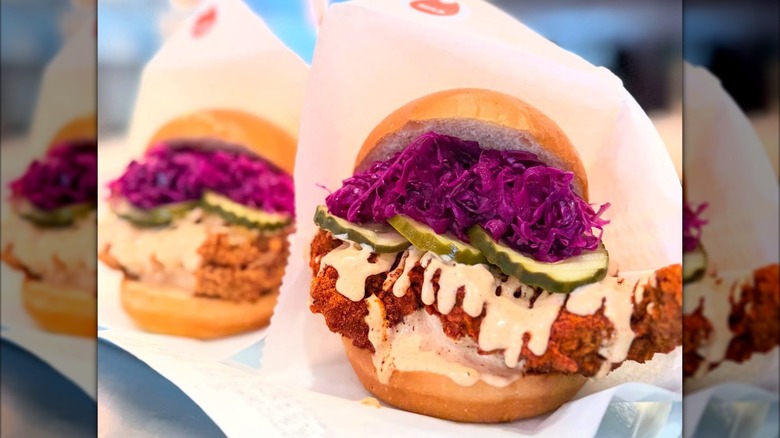 Two fried chicken sandwiches topped with pickles, bright purple slaw, and creamy sauce