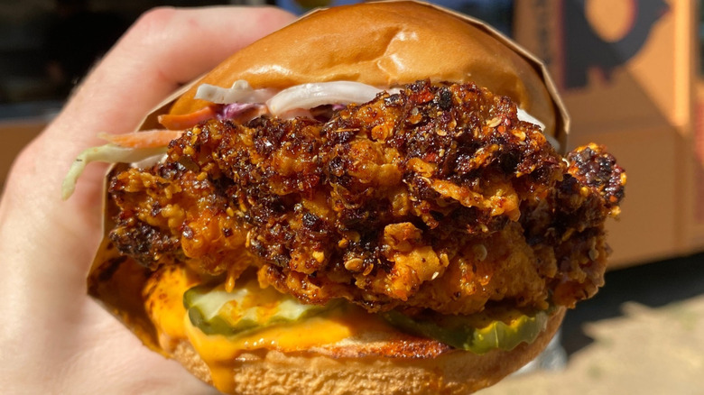 Someone holding a crispy fried chicken sandwich with pickles, sauce, and coleslaw