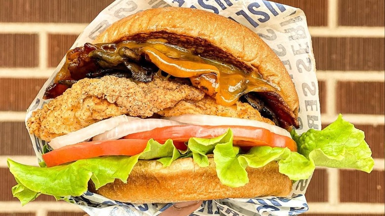 fried chicken sandwich layered with lettuce, tomato, onions, cheese, and bacon