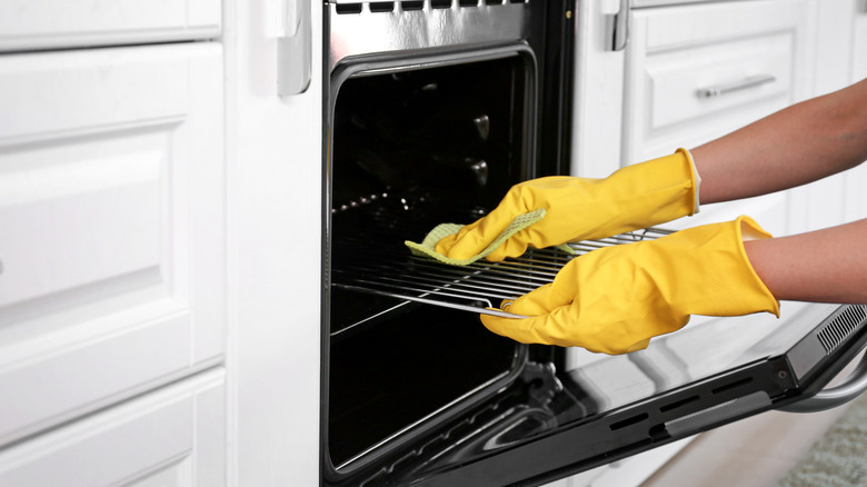 Hands in yellow gloves cleaning oven
