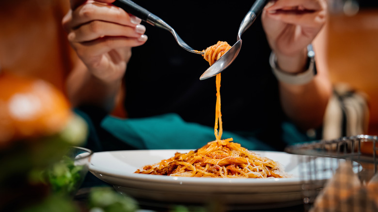 Person eating a plate of spaghetti with a spoon and fork