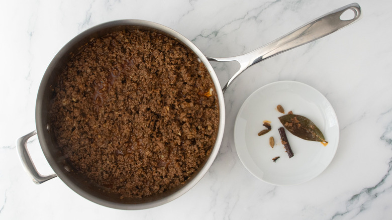 Ground beef in pan next to whole spices on plate