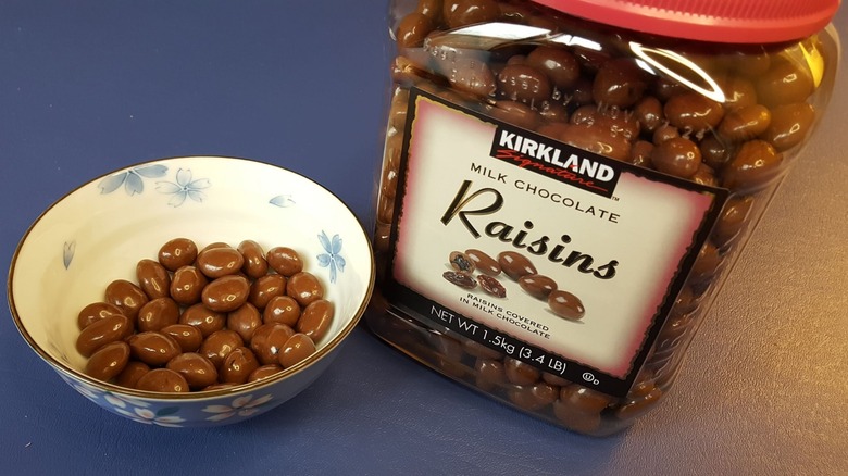 Kirkland Signature chocolate-covered raisins in a bowl, next to a tub of the snack.