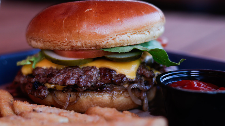 Closeup of burger with onions, pickles, lettuce, and tomato.