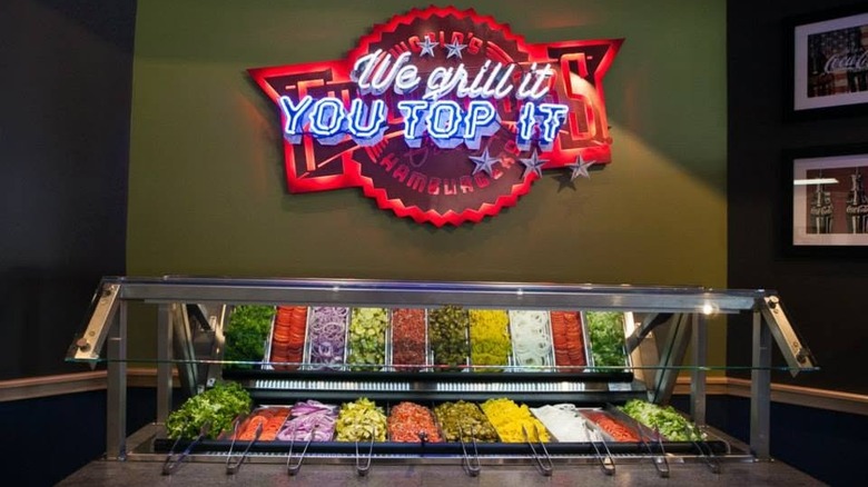Neon sign above Fuddruckers burger toppings bar