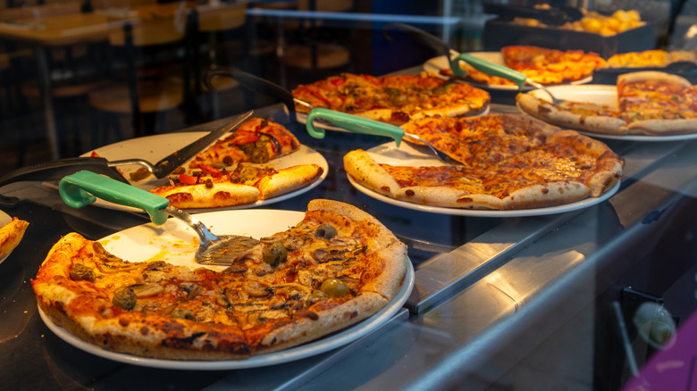 Several pizzas under warming lamp in restaurant buffet.