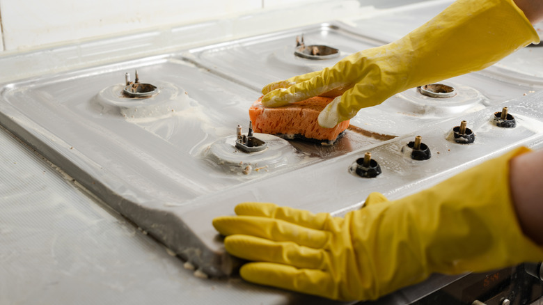 Hands wearing gloves cleaning a stovetop with a sponge