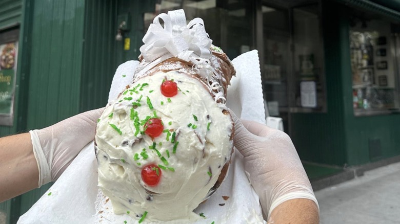 Gloved hands holding giant cannolo in front of Circo's Pastry Shop.