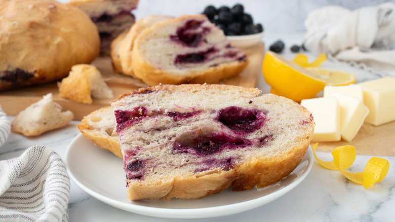 Slices of lemon blueberry bread on plate with more bread, butter, and lemons in background