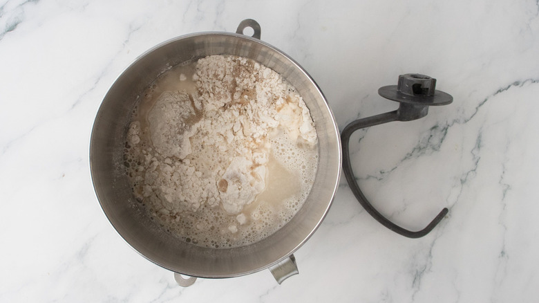 Unmixed bread dough ingredients in bowl next to dough hook attachment