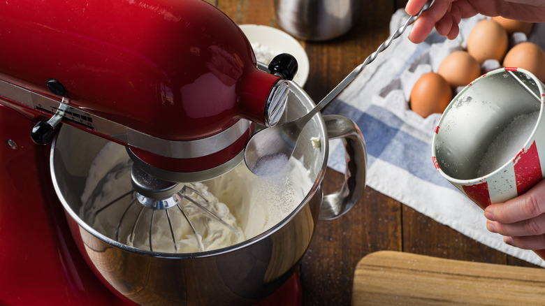 Person spooning sugar into Kitchenaid stand mixer with whisk attachment