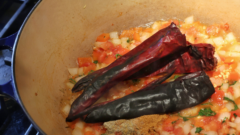 toasted chiles and spices in a pot atop chopped vegetables