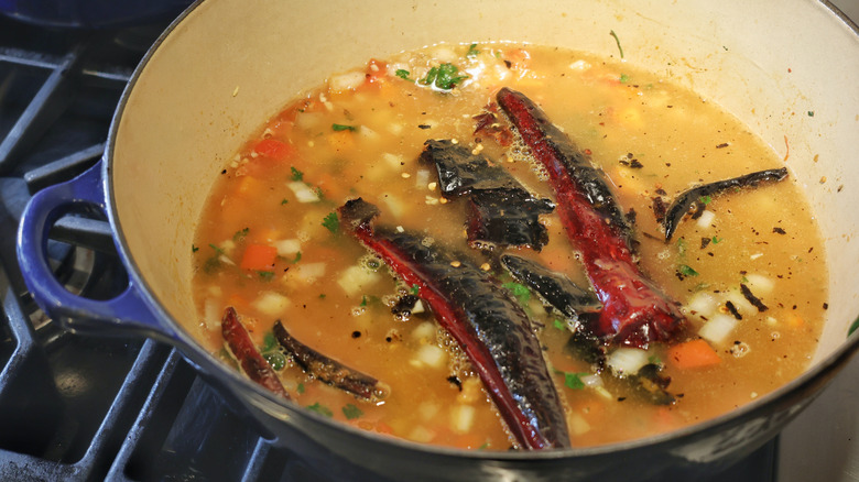 chopped vegetables and toasted chiles floating in pot of broth