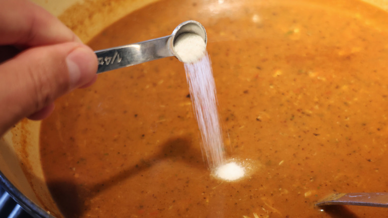 sugar pouring from small metal measuring spoon into pot of chilpachole