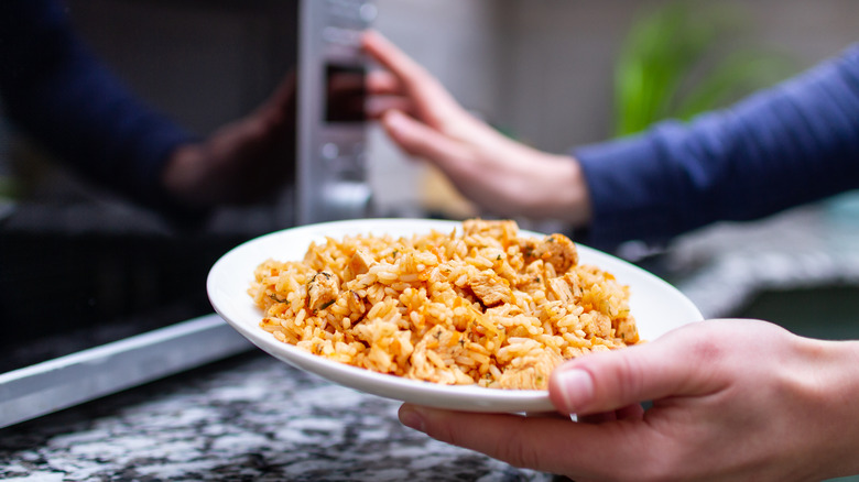 woman's hand holding bowl of rice to go in the microwave 