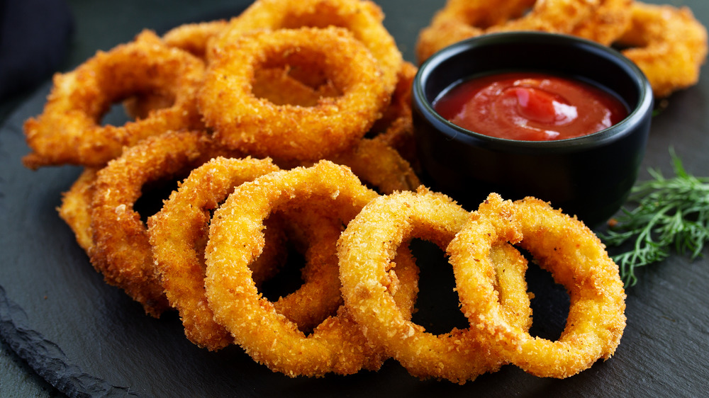 Onion rings on a black board with a cup of ketchup