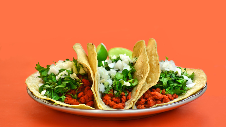 Plate with three corn tacos on orange background