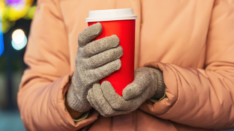 Gloved hands holding paper coffee cup