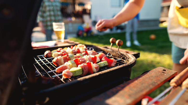 A person grilling kebabs on a black grill