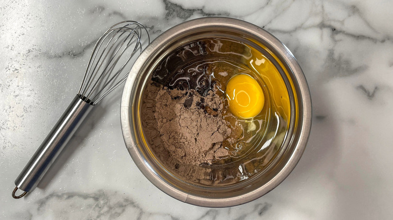 Egg and chocolate cake mix in bowl next to whisk