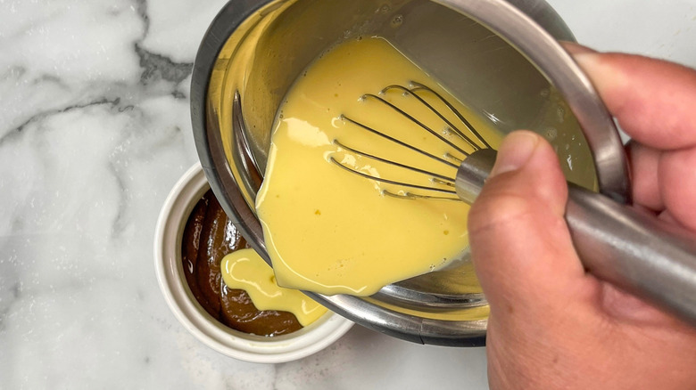 Flan mixture in bowl pouring into ramekin with cake batter