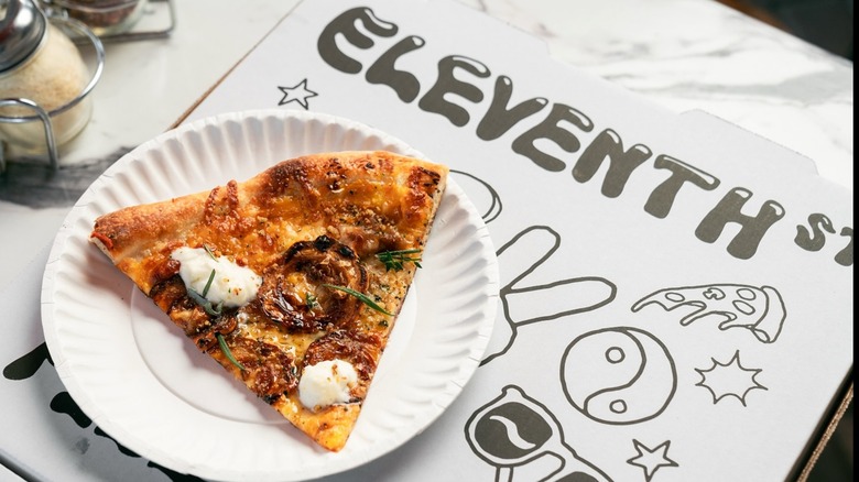 slice of pizza on paper plate atop eleventh street pizza box