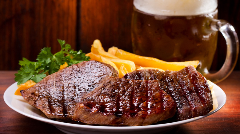 Steak, fries, and a mug of beer with wooden paneling in background