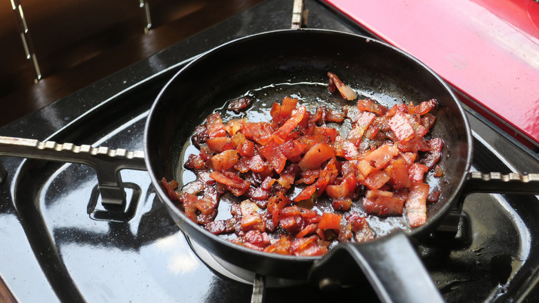 Bacon slices frying on a cast iron pan.