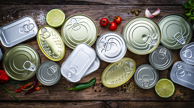 Canned foods on wooden table with vegetables and peppers