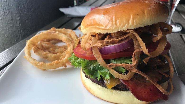 Large burger on a plate with crispy fried onions.