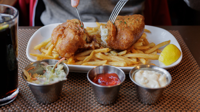 Person using fork and knife to eat fish and chips in restaurant