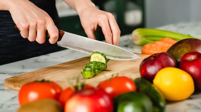 A person cutting a cucumber on a wooden cutting board