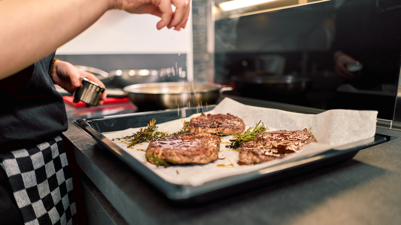 Homecook sprinkling salt over steaks on parchment-lined sheetpan.