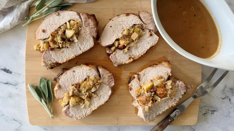 Pear and hazelnut stuffed pork loin pieces on wooden board with gravy boat
