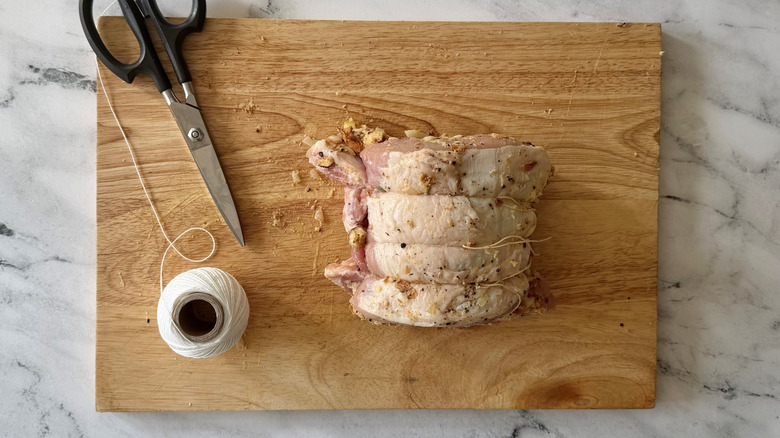Rolled up pork loin on wooden board with kitchen twine and scissors