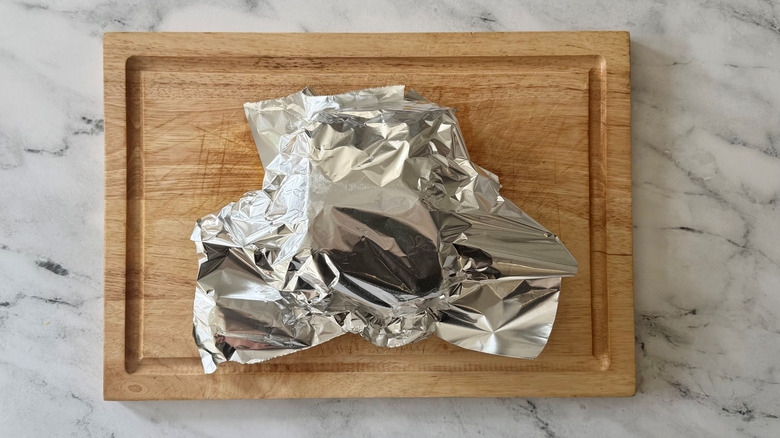 Pork loin tented with foil on wooden board