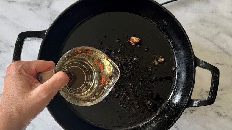 Hand holding measuring cup of cider over skillet