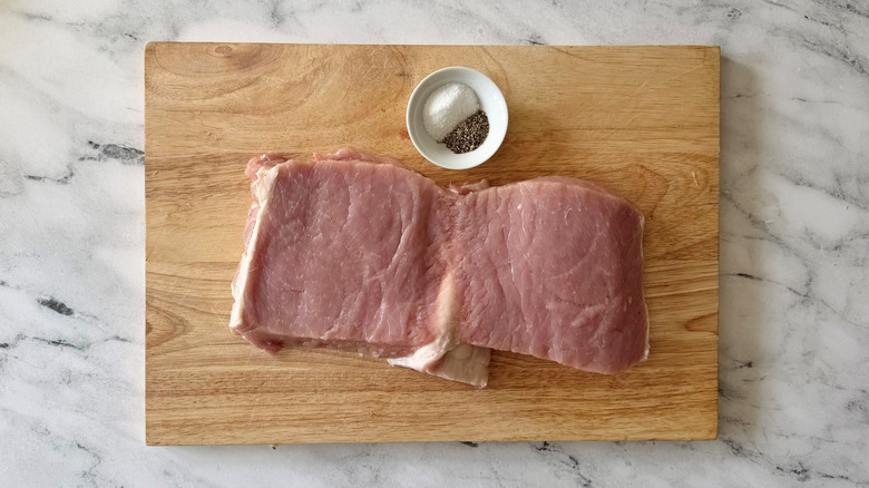 Butterflied pork loin with salt and pepper on wooden board