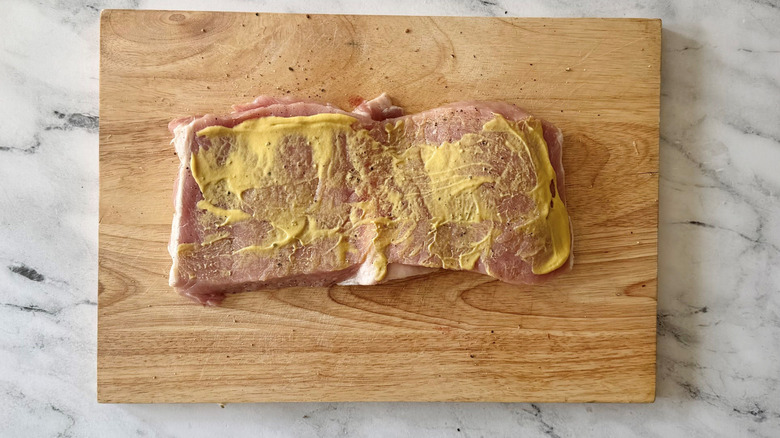 Pork loin coated in Dijon mustard on wooden board