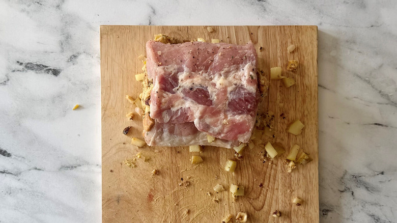 Rolled up and stuffed pork loin with loose pieces of pear on wooden board