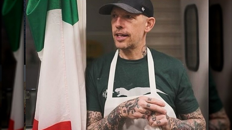 Anthony Mangieri in a ballcap, green shirt, and apron, leaning against wall