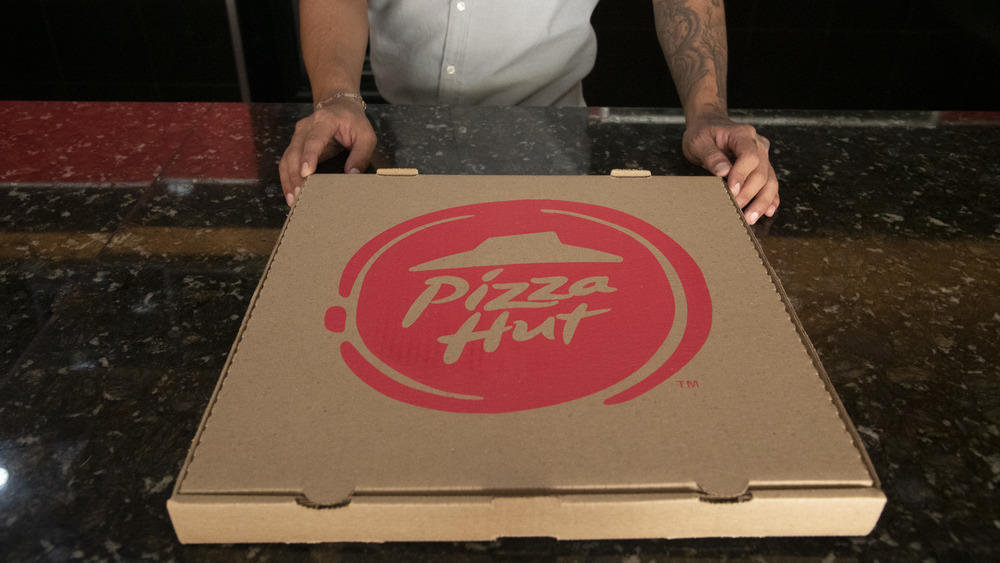 Hands pushing a Pizza Hut Pizza box forward