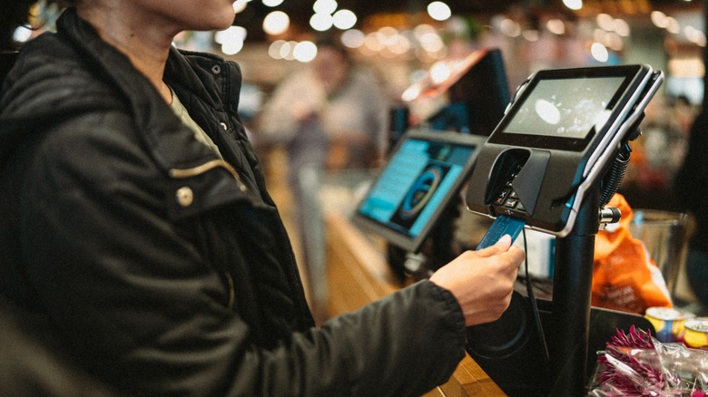 Customer with black coat paying with a blue credit card at a supermarket register