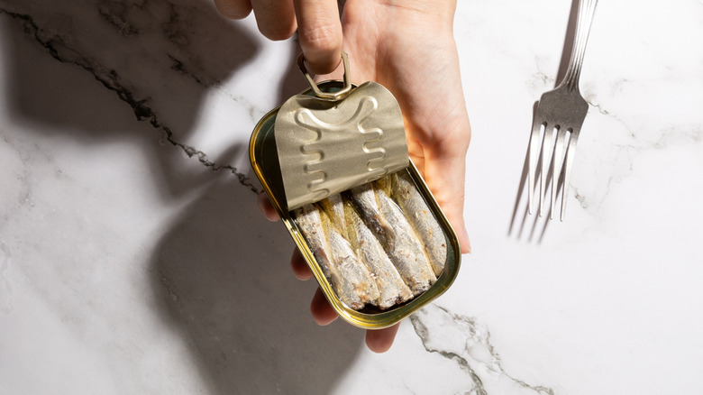 Hand opening can of sardines in oil.